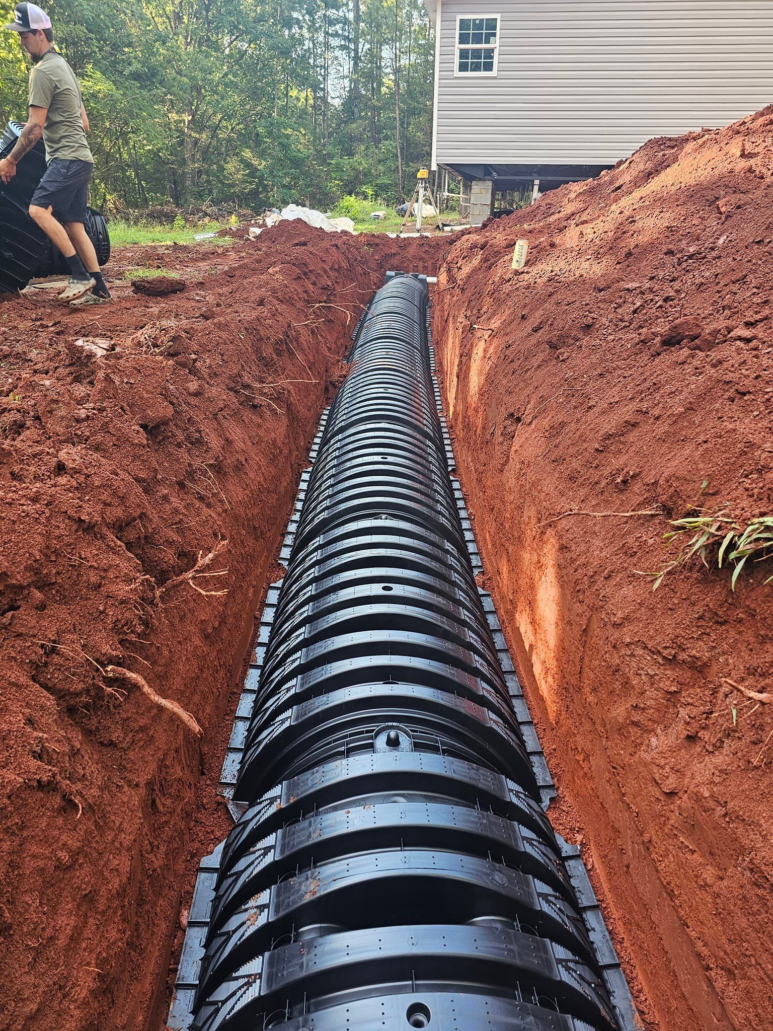 A large black pipe is being installed in a trench next to a house.