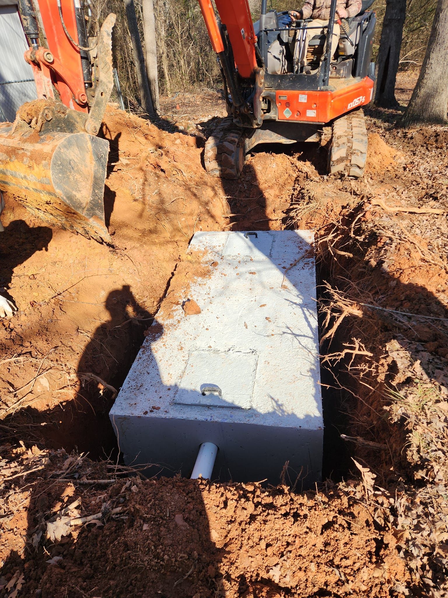 A large concrete box is sitting in the dirt next to an excavator.