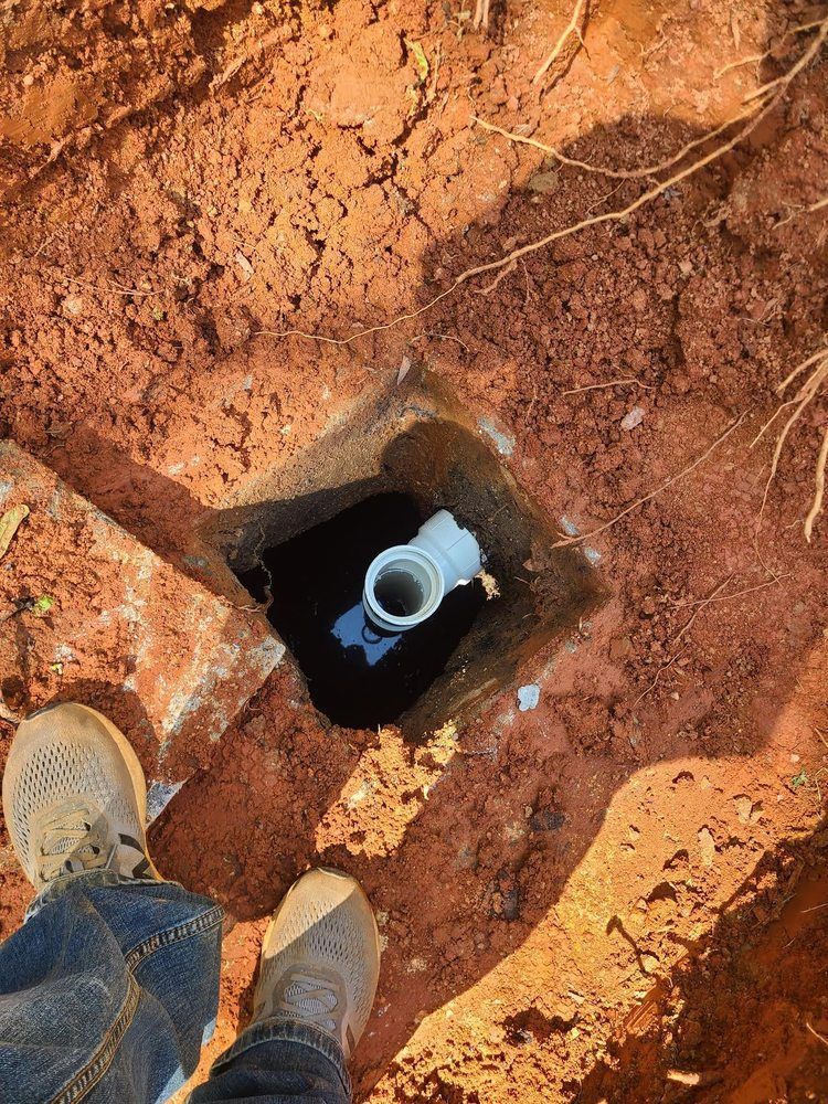 A person is standing next to a hole in the ground with a pipe in it.