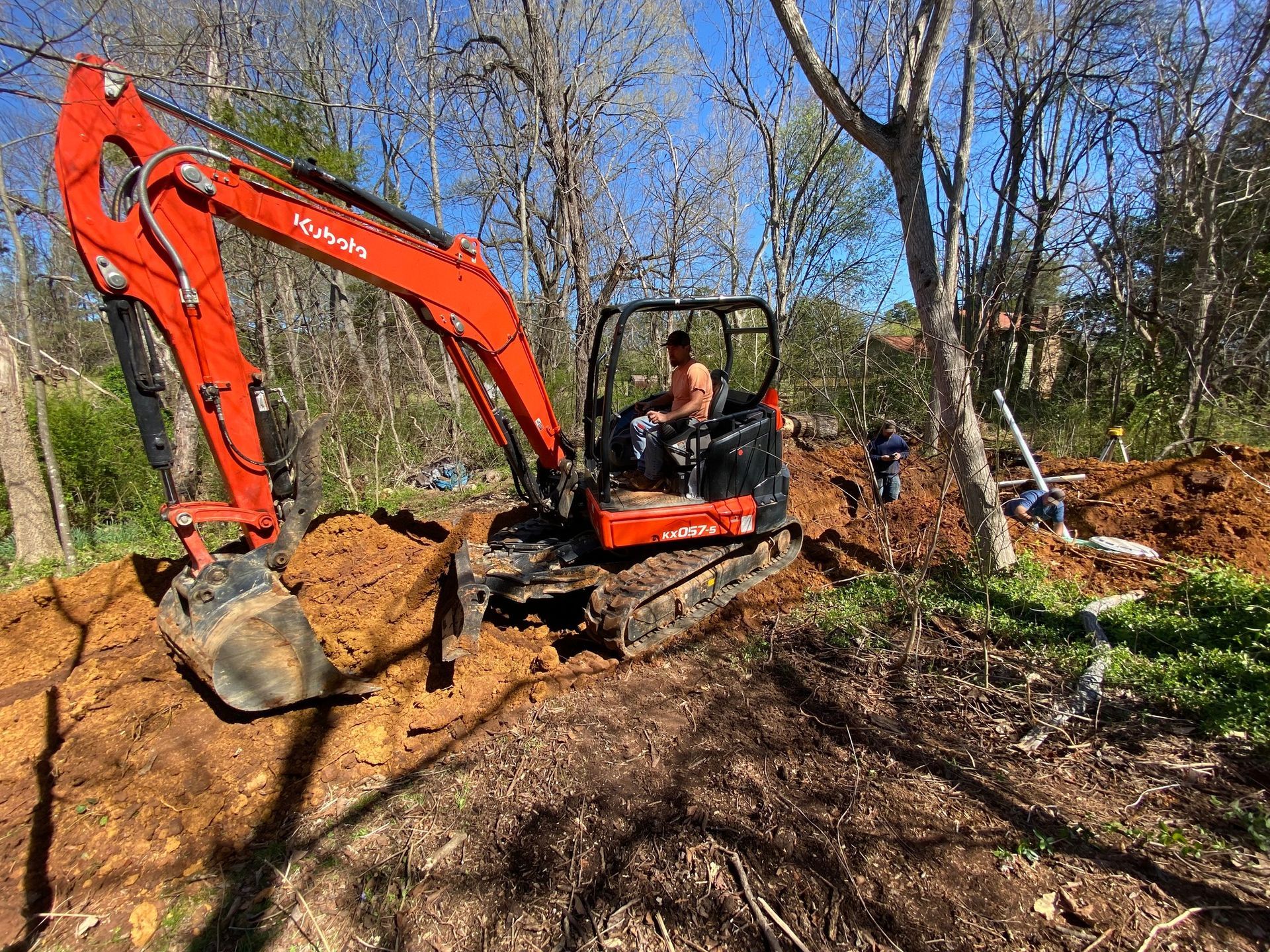 A man is driving a red excavator in a dirt field.