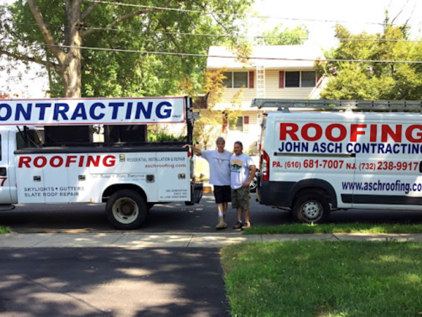 Two roofing trucks are parked next to each other
