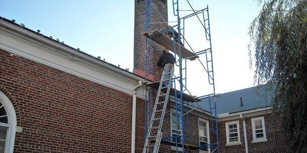 A man is standing on a ladder in front of a brick building.