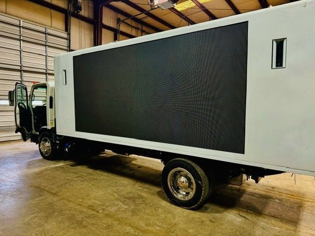 A white truck with a large screen on the side is parked in a garage.