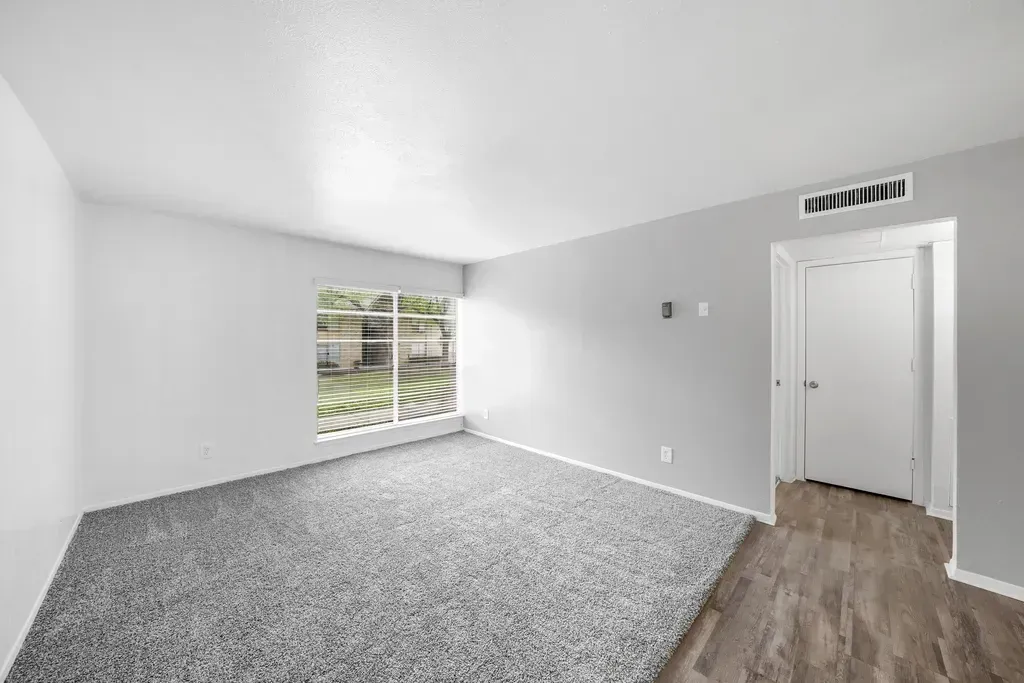 An empty living room with a carpeted floor and a window.