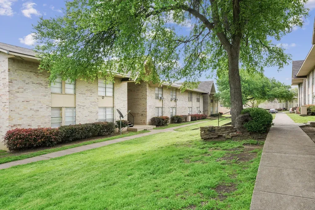 A brick apartment building with a lush green lawn and a tree in front of it.