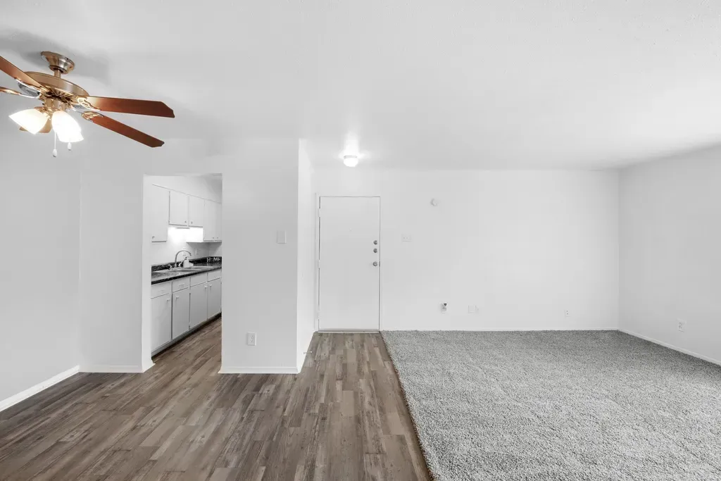 An empty living room with a ceiling fan and hardwood floors.