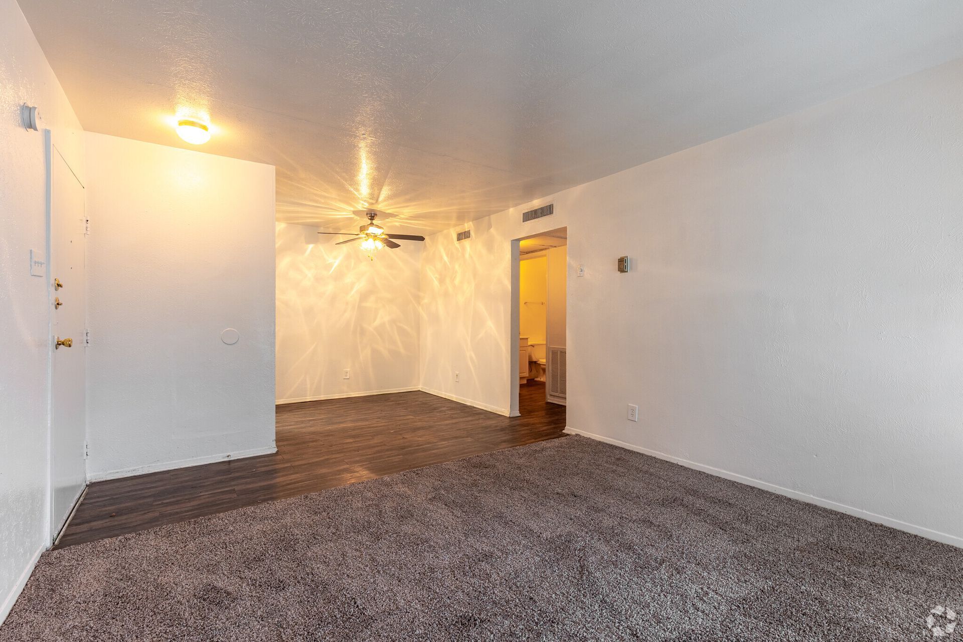 An empty living room with a ceiling fan and a carpeted floor.