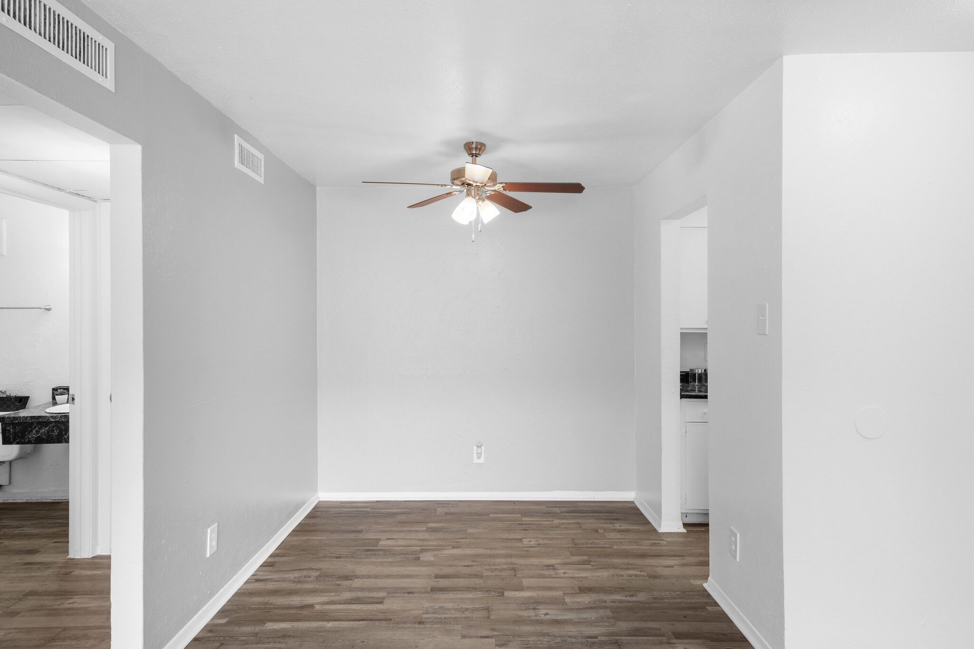 An empty dining room with hardwood floors and a ceiling fan.