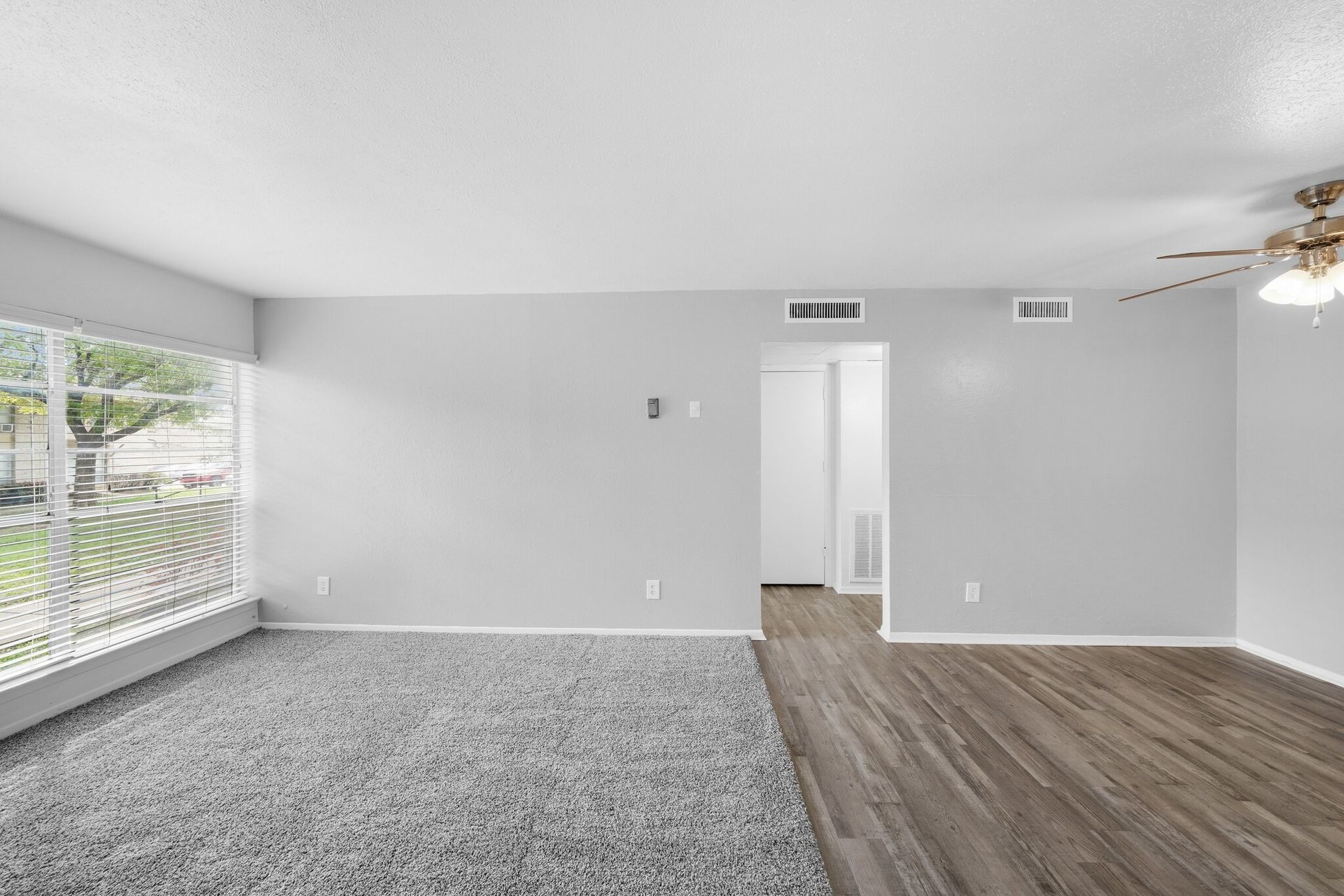 An empty living room with a ceiling fan and a large window.
