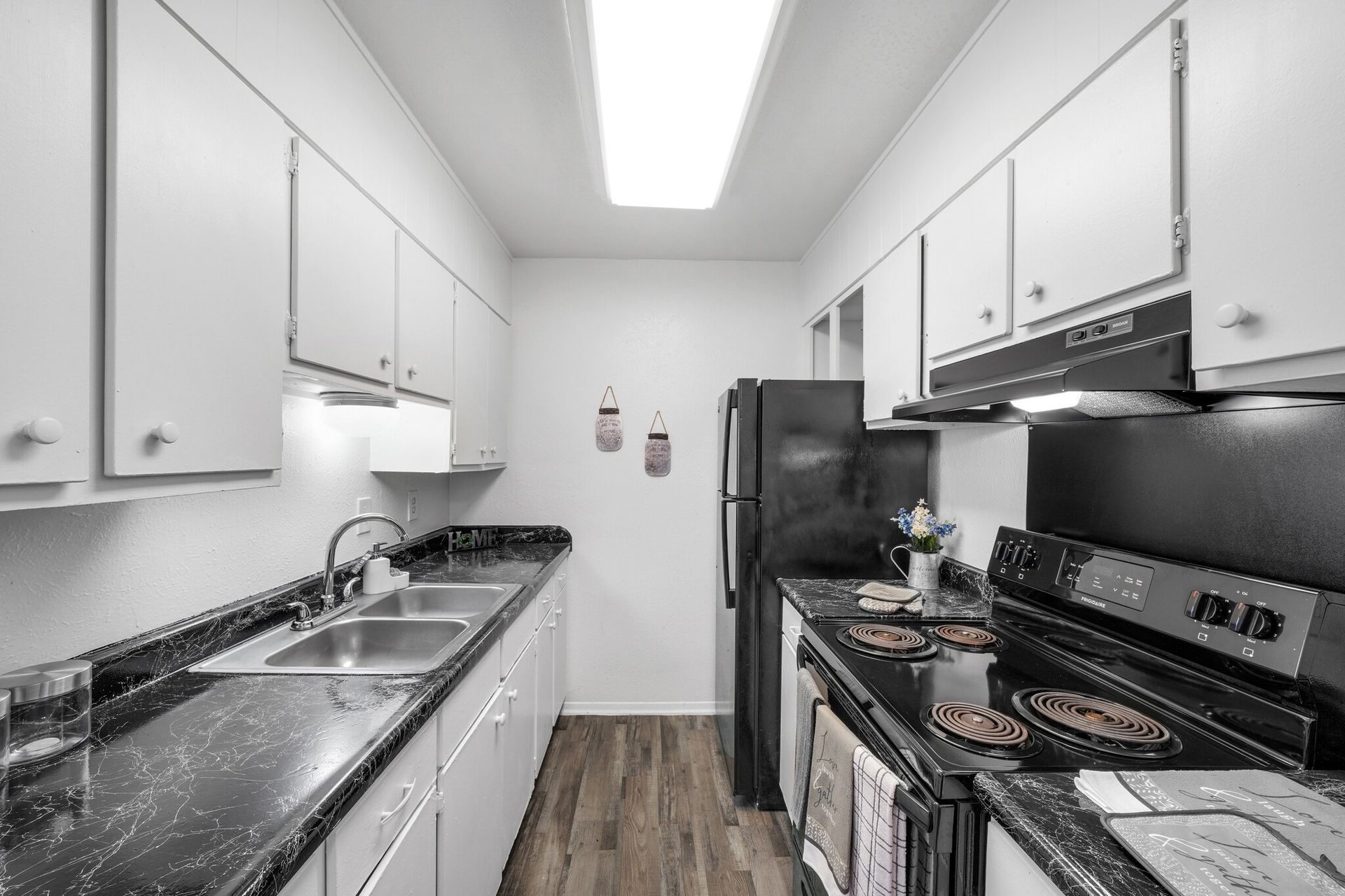 A kitchen with white cabinets , black counter tops , a stove and a refrigerator.