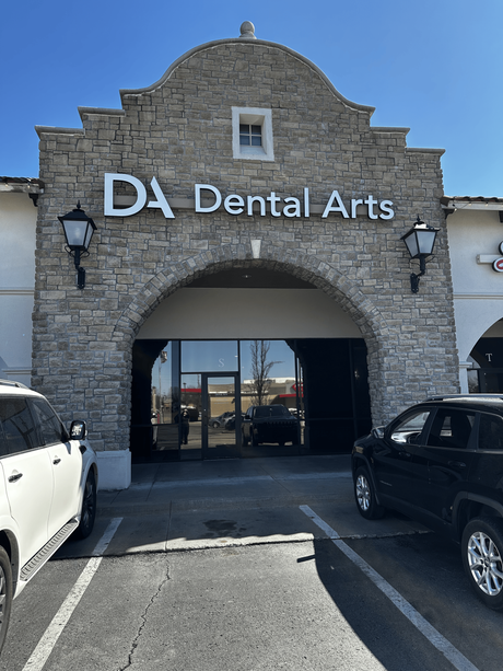 A dental arts building with cars parked in front of it.