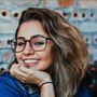 A woman wearing glasses is smiling with her hand on her chin.