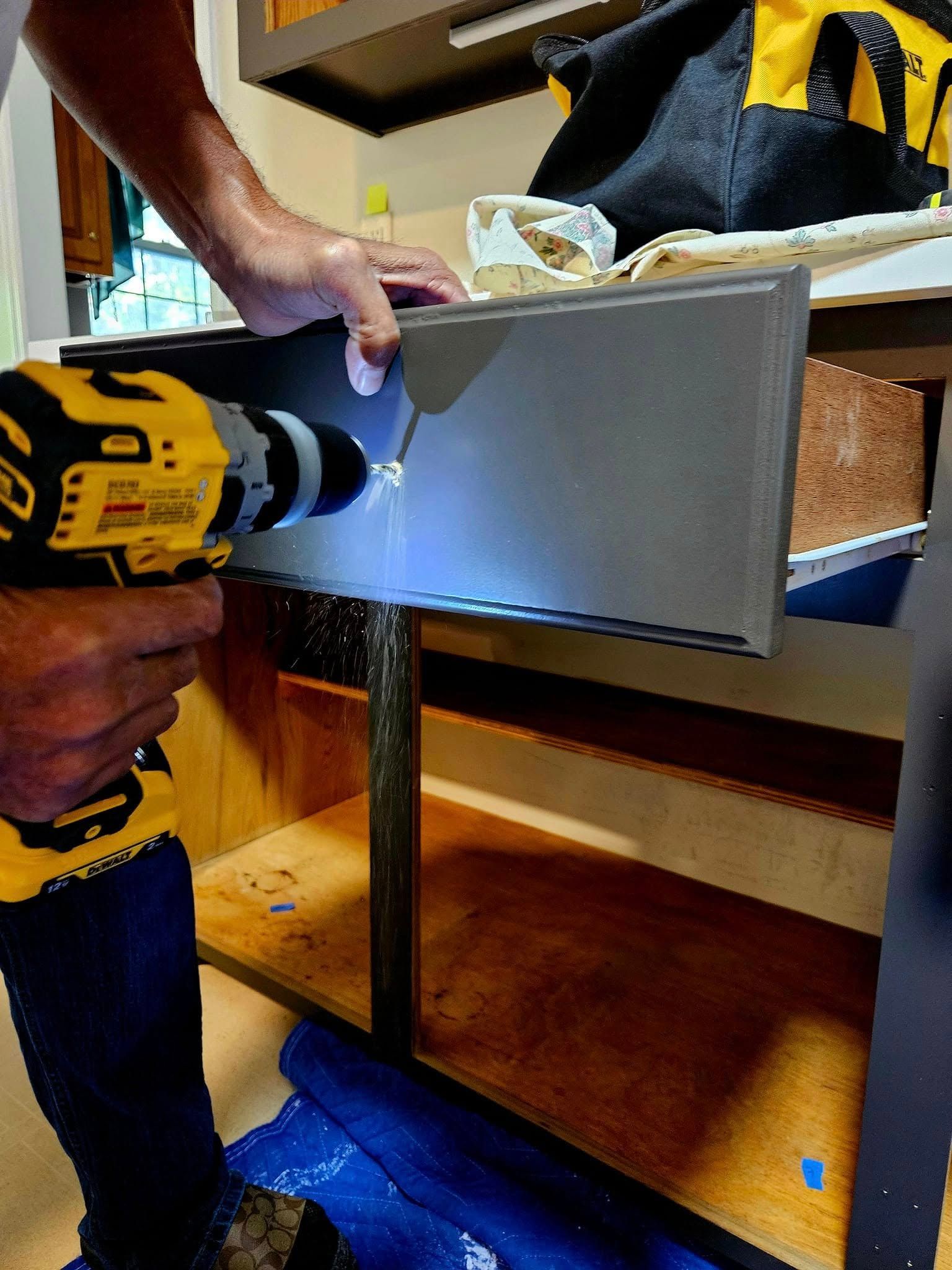 A man is using a drill to fix a drawer in a kitchen.