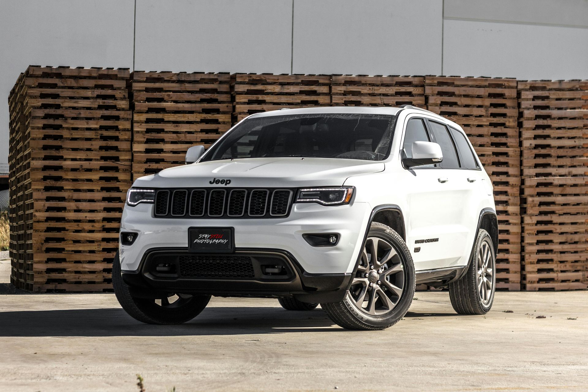 White Jeep Grand Cherokee SUV with dark wheels in front of stacked wooden pallets.