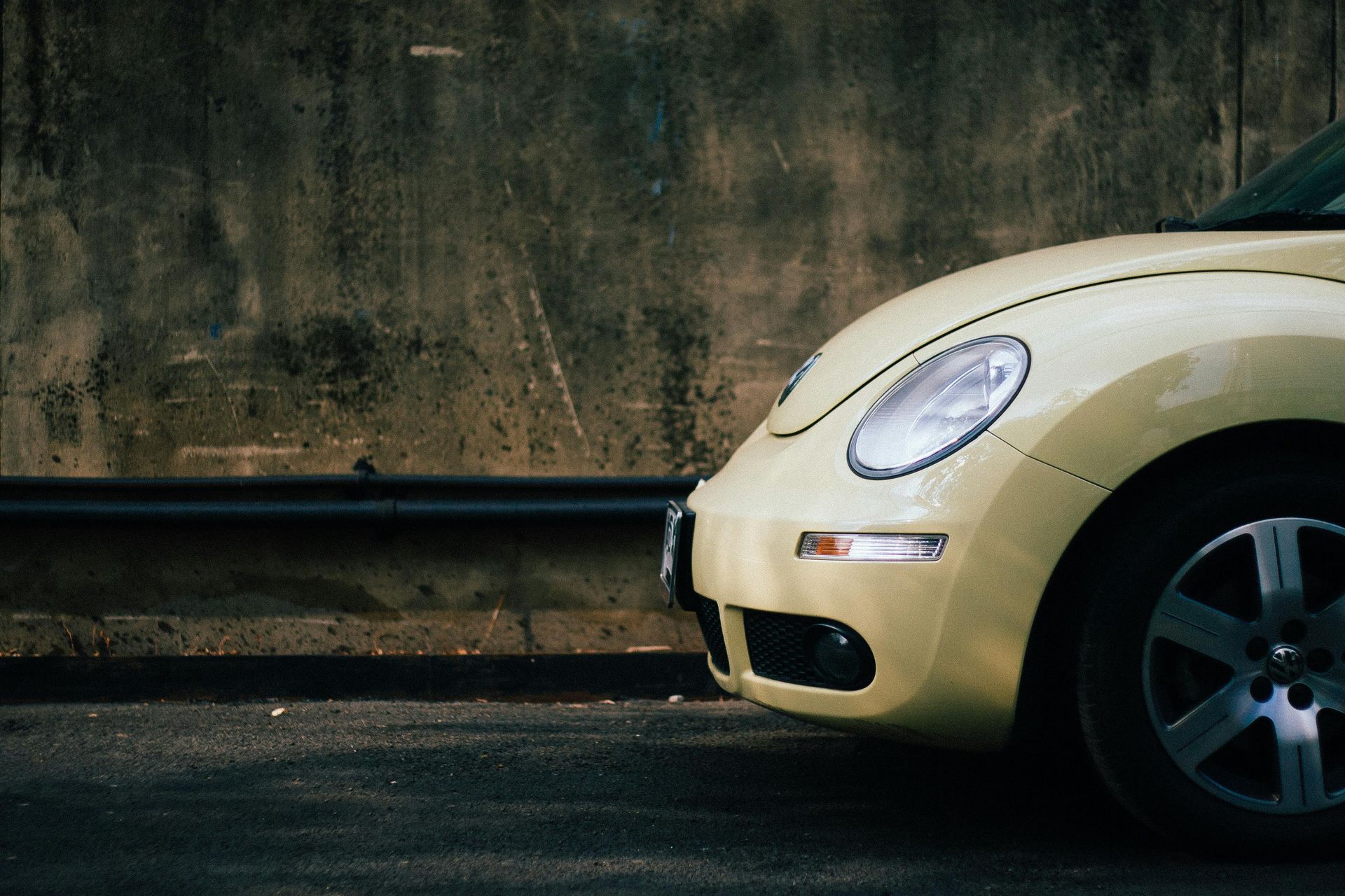 Yellow Volkswagen Beetle parked next to a weathered concrete wall.