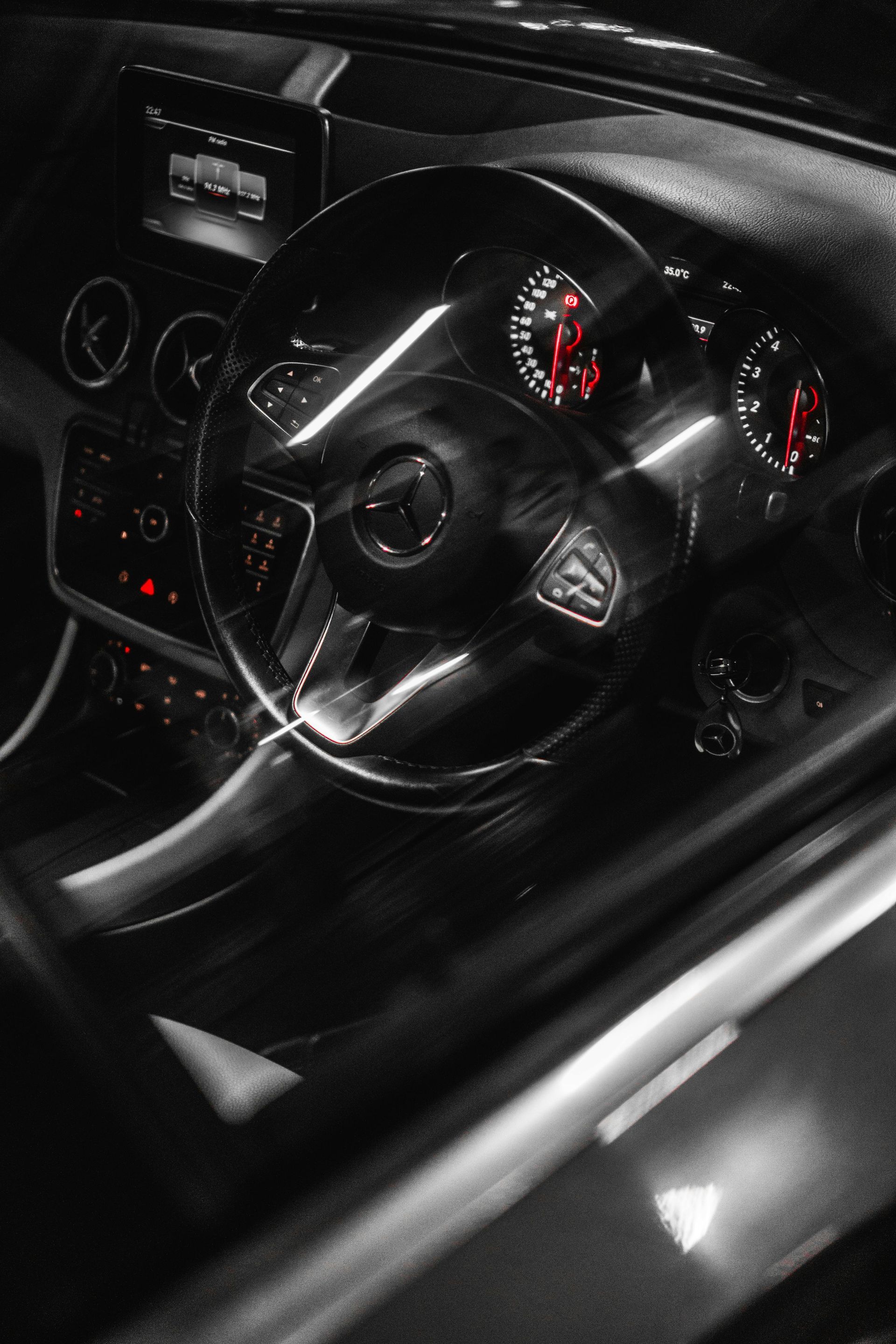 Black and white car interior. Dashboard with a steering wheel and illuminated gauges.