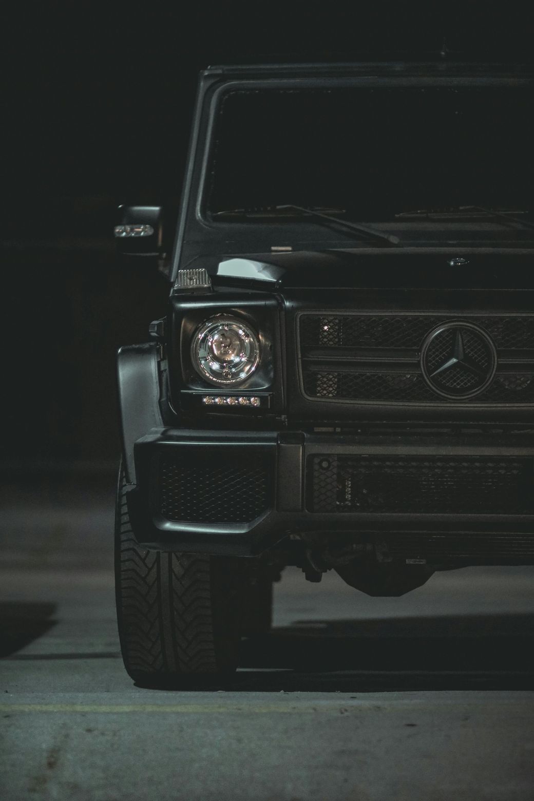 Black Mercedes-Benz G-Class SUV, front view, parked in dark setting.
