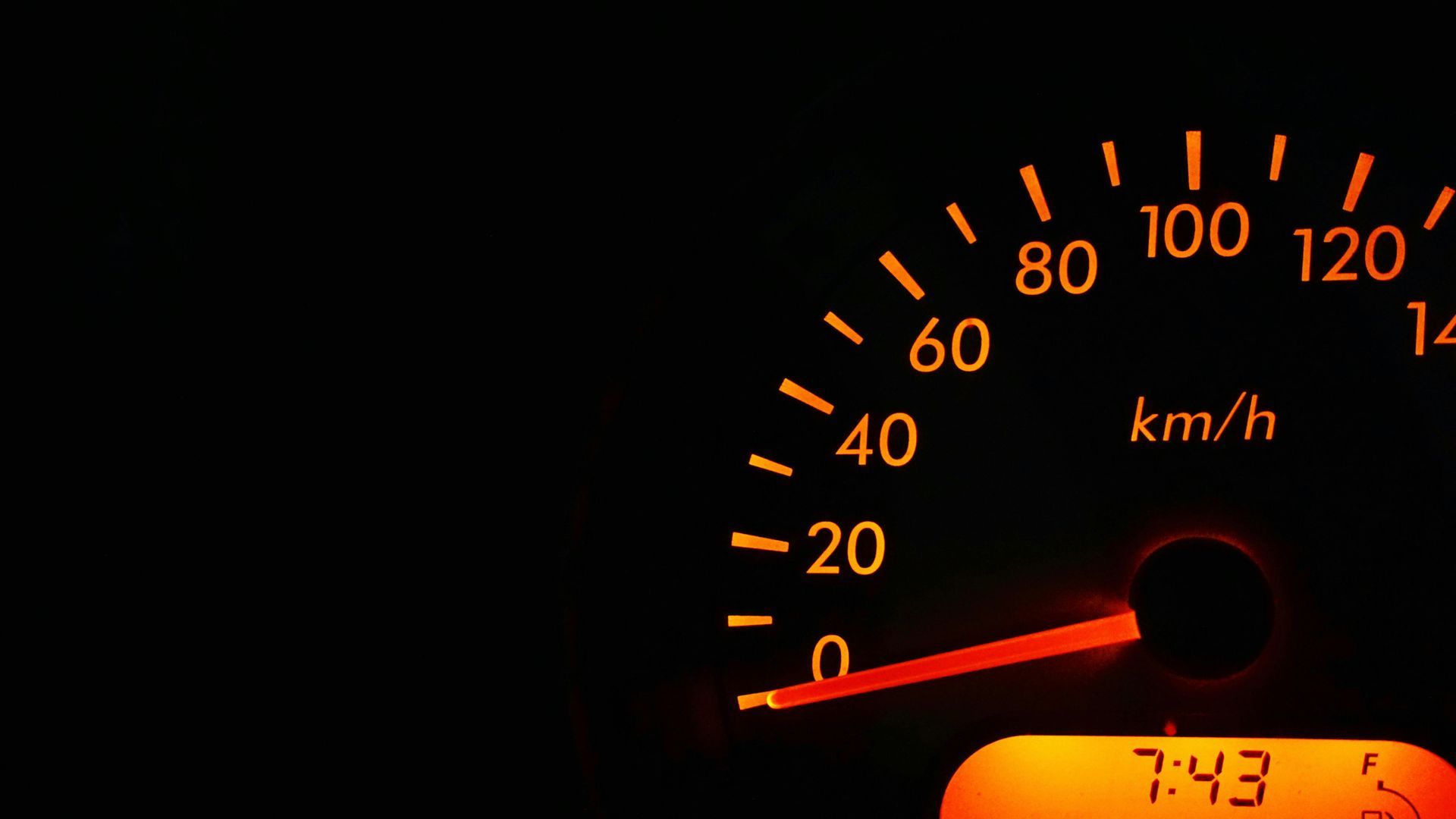 Orange-lit car speedometer at 10 km/h, with a digital clock displaying 7:43.