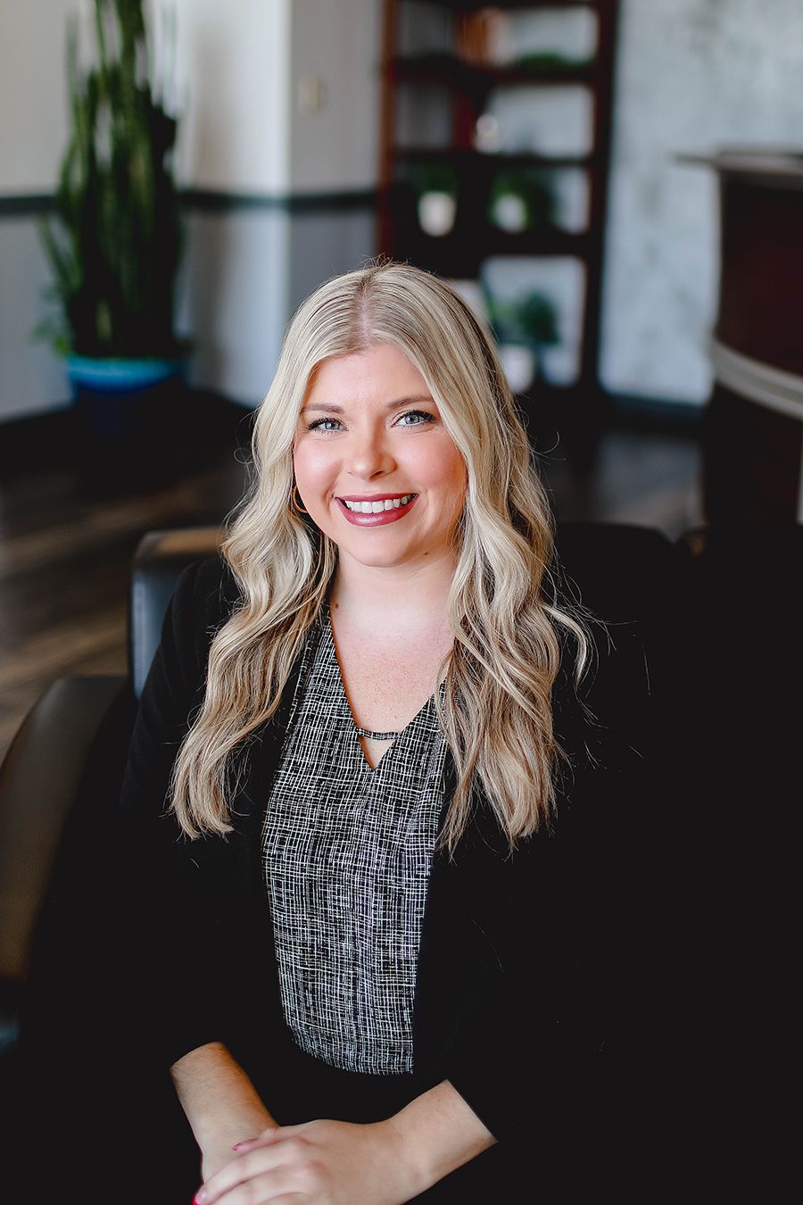 A woman in a pink jacket is sitting on a couch with her hands on her hips.