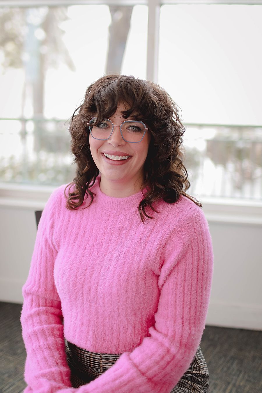 A woman wearing glasses and a red sweater is smiling for the camera.