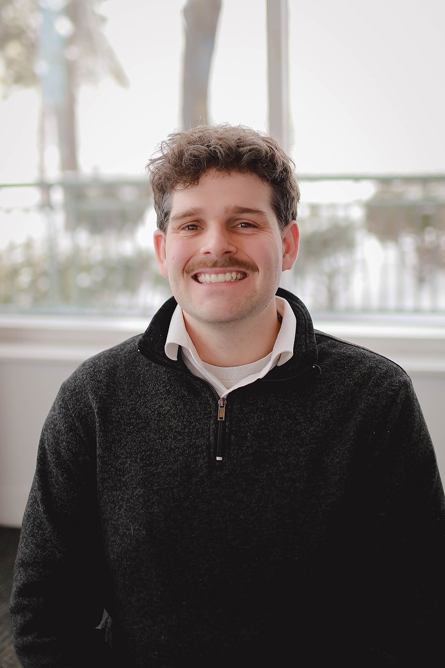 A man in a white shirt is smiling for the camera while sitting in a chair.
