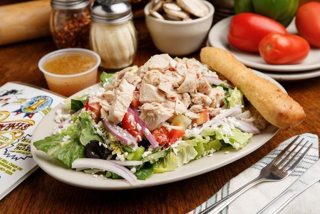 A salad with chicken , lettuce , tomatoes , onions and olives on a plate on a table.