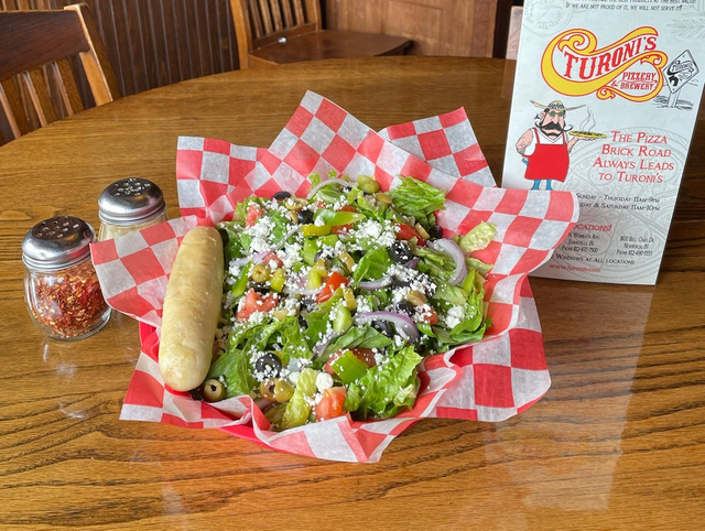 A salad and a loaf of bread are on a checkered paper on a table.