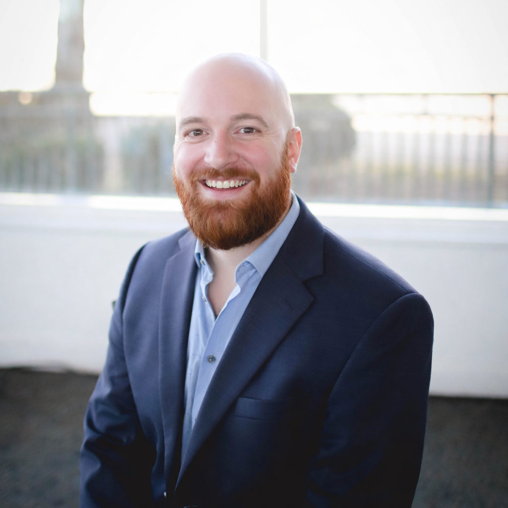 A man with a beard is wearing a blue shirt and smiling for the camera.