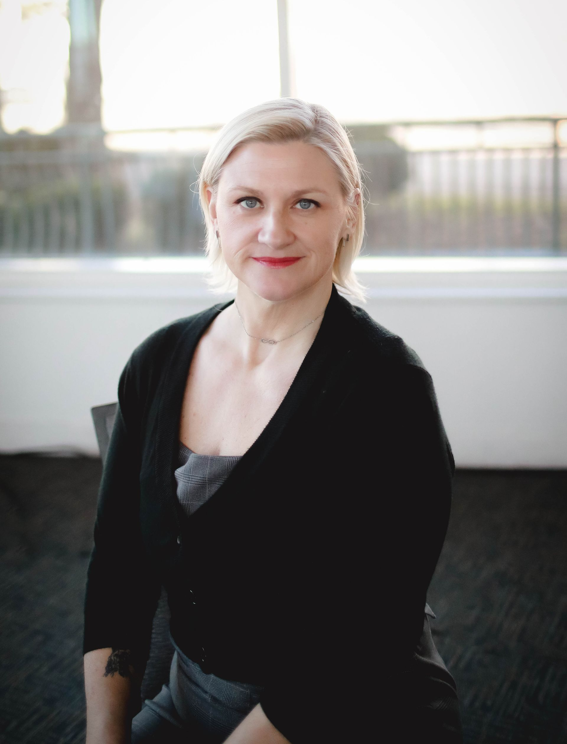 A woman with blonde hair is wearing a black shirt and a necklace.
