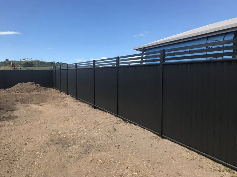 A black fence is surrounding a dirt field in front of a house. — DC Fencing In Wondunna, QLD
