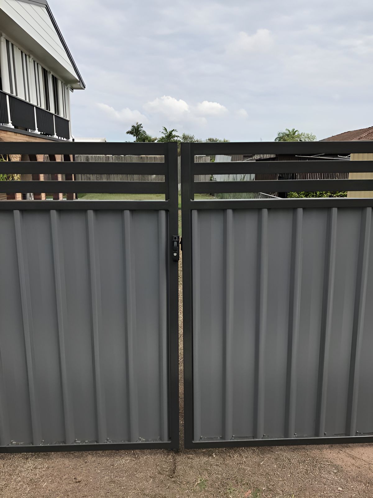 A Gray Metal Gate With a Black Frame is Sitting in Front of a House — DC Fencing In Wondunna, QLD