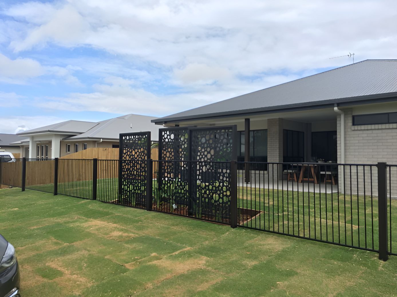 A Black Fence is in Front of a House in a Residential Area — DC Fencing In Wondunna, QLD