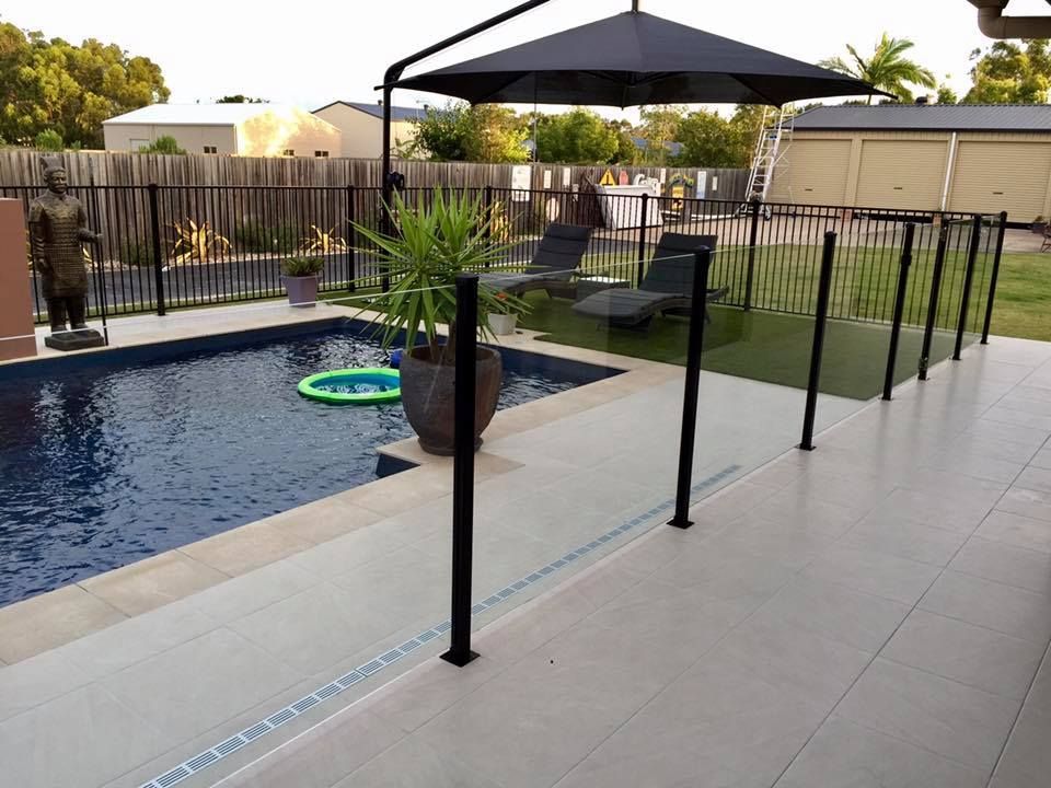 A Swimming Pool With a Black Umbrella and Chairs — DC Fencing In Wondunna, QLD