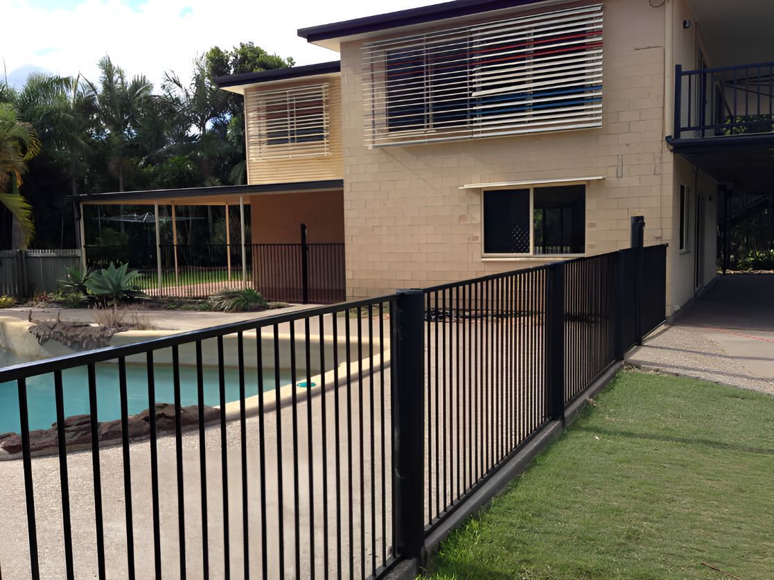 A Fence Surrounds a Swimming Pool in Front of a House — DC Fencing In Wondunna, QLD