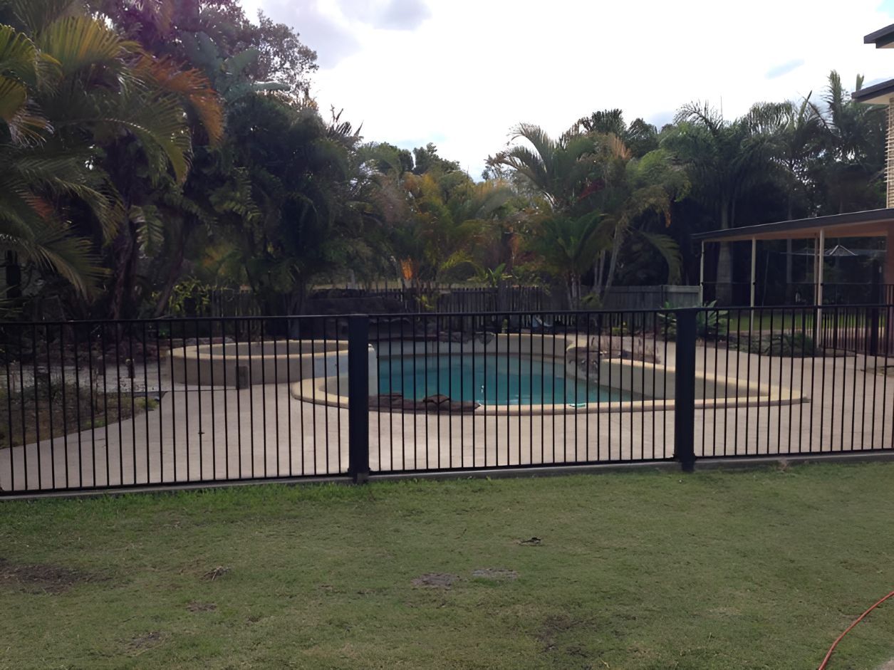 A Black Fence Surrounds a Swimming Pool in a Backyard — DC Fencing In Wondunna, QLD