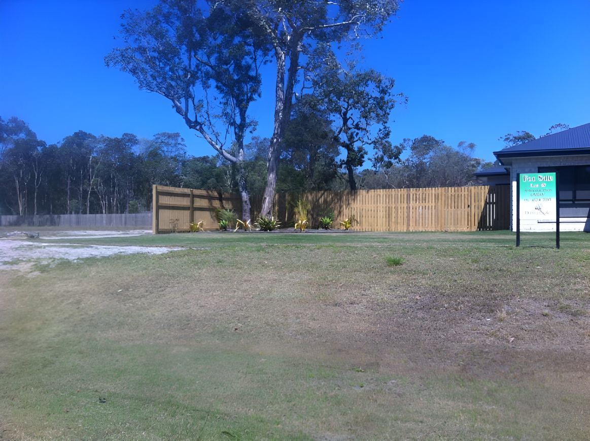 A Wooden Fence Surrounds a Grassy Field With a House in the Background — DC Fencing In Wondunna, QLD