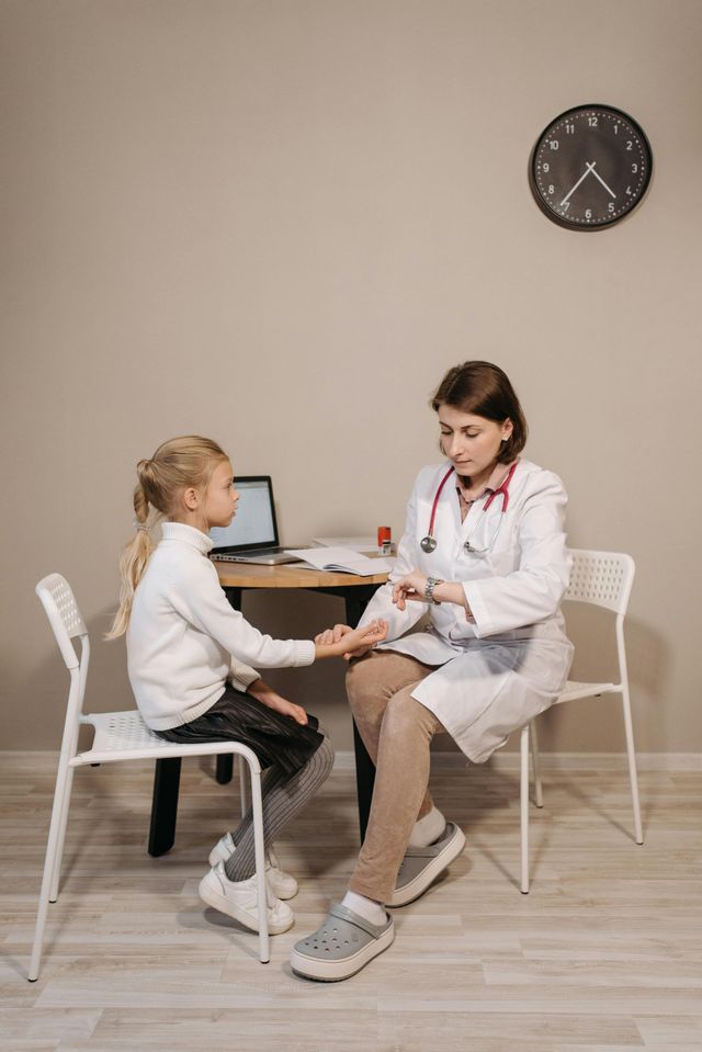 Doctor examining a young girl's hand. Both are seated in a medical office.