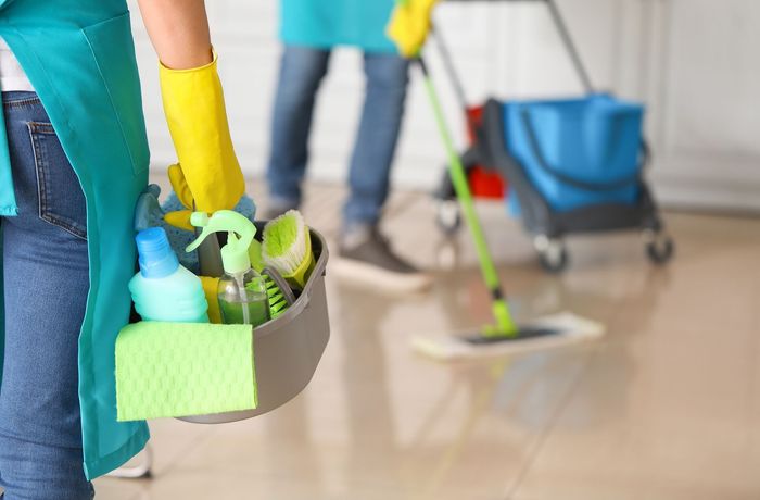 A woman is holding a bucket of cleaning supplies.