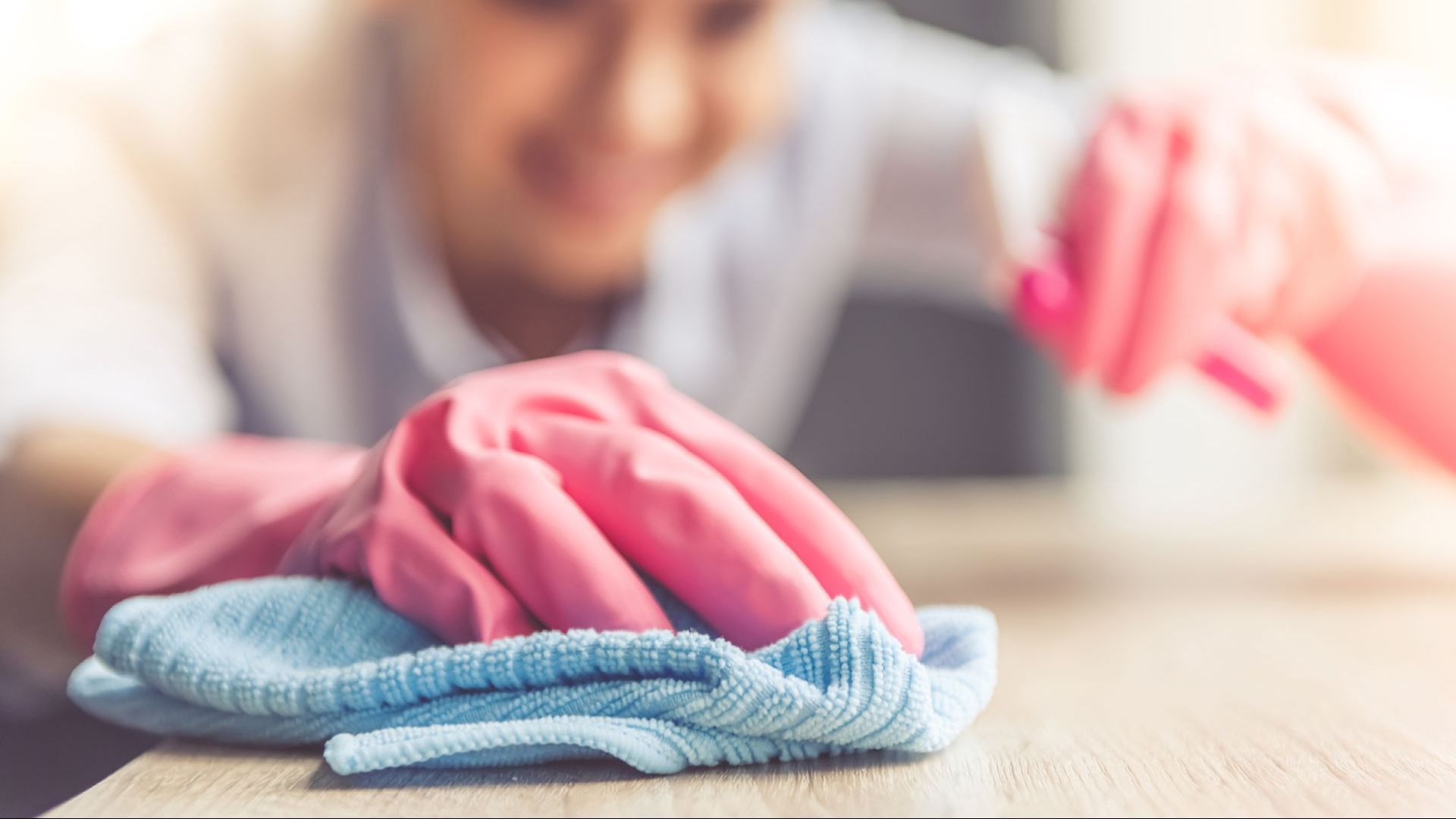 A woman wearing pink gloves is cleaning a table with a cloth.