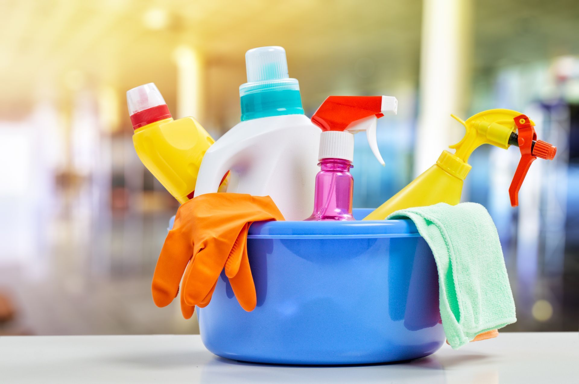 A blue bucket filled with cleaning supplies and gloves on a table.