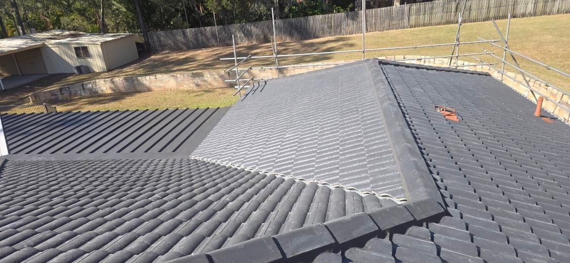 View of a dark gray tiled roof with a small building and fence in the background. — Boostn Pty Ltd in Maryborough, QLD