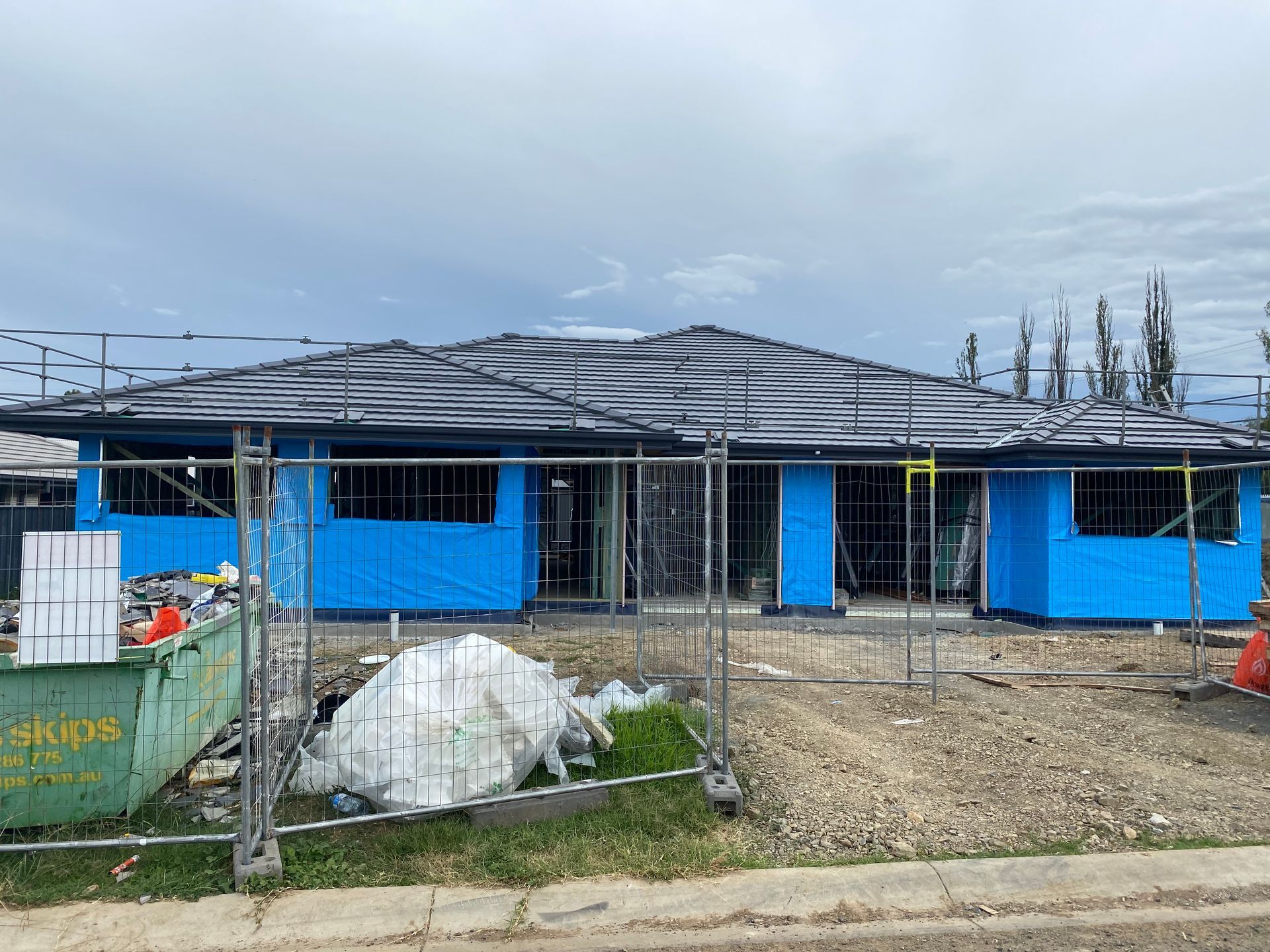 Construction site with two houses framed, blue wrap, under dark tarps, overcast sky. — Boostn Pty Ltd in Glastonbury, QLD