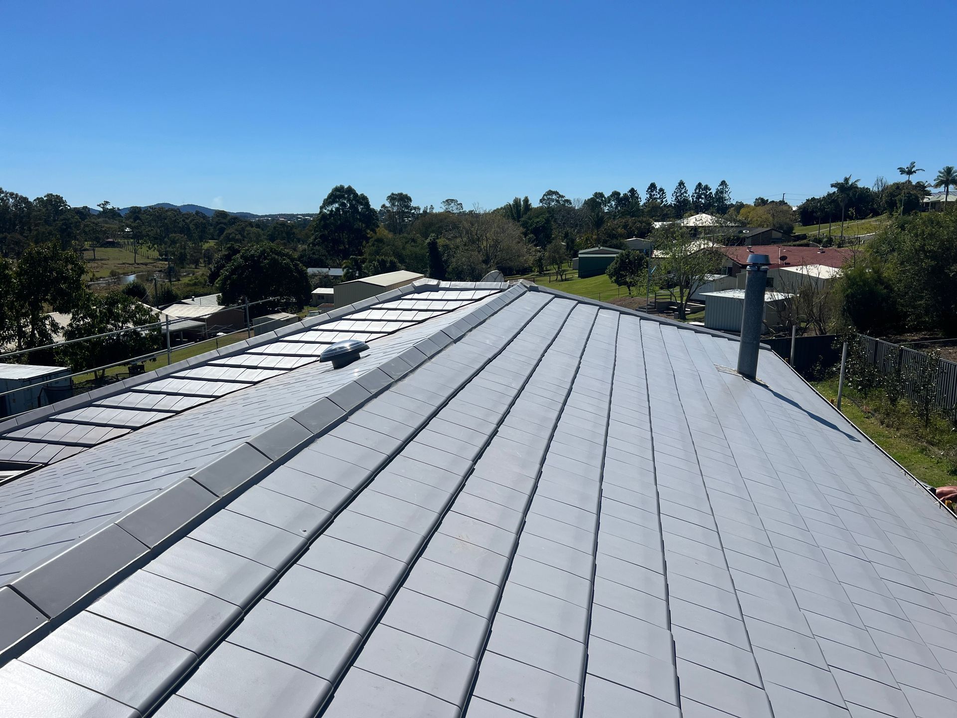 View of a silver metal roof on a building, with a blue sky and trees in the background. — Boostn Pty Ltd in Tin Can Bay, QLD