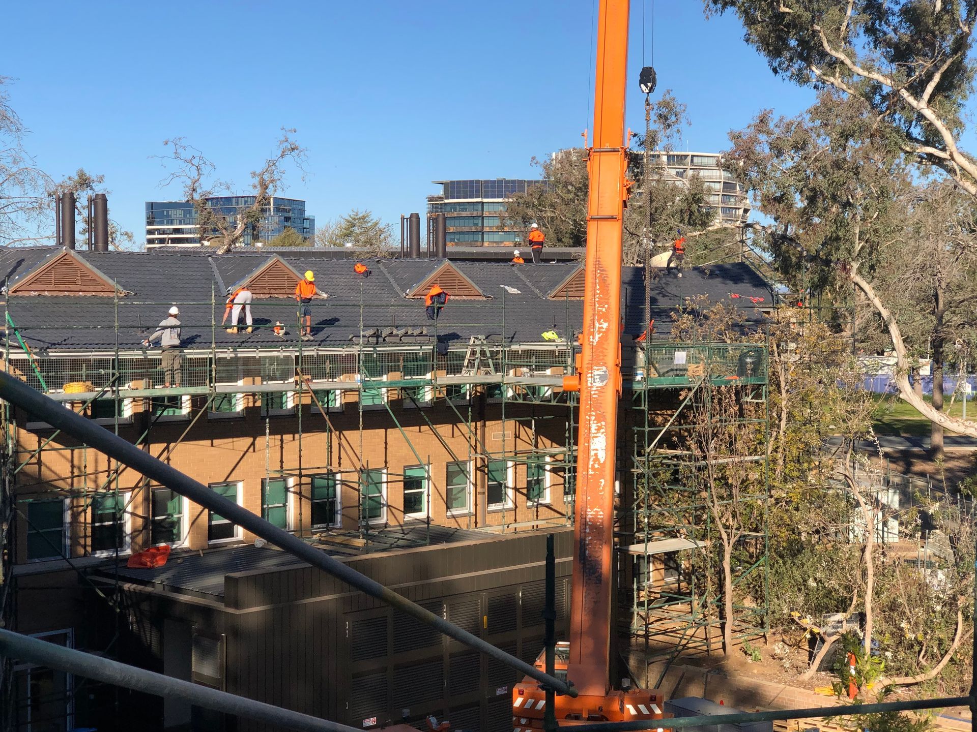 Crane lifting materials to construction workers on a building's roof, with trees and other buildings in the background. — Boostn Pty Ltd in Glastonbury, QLD 
