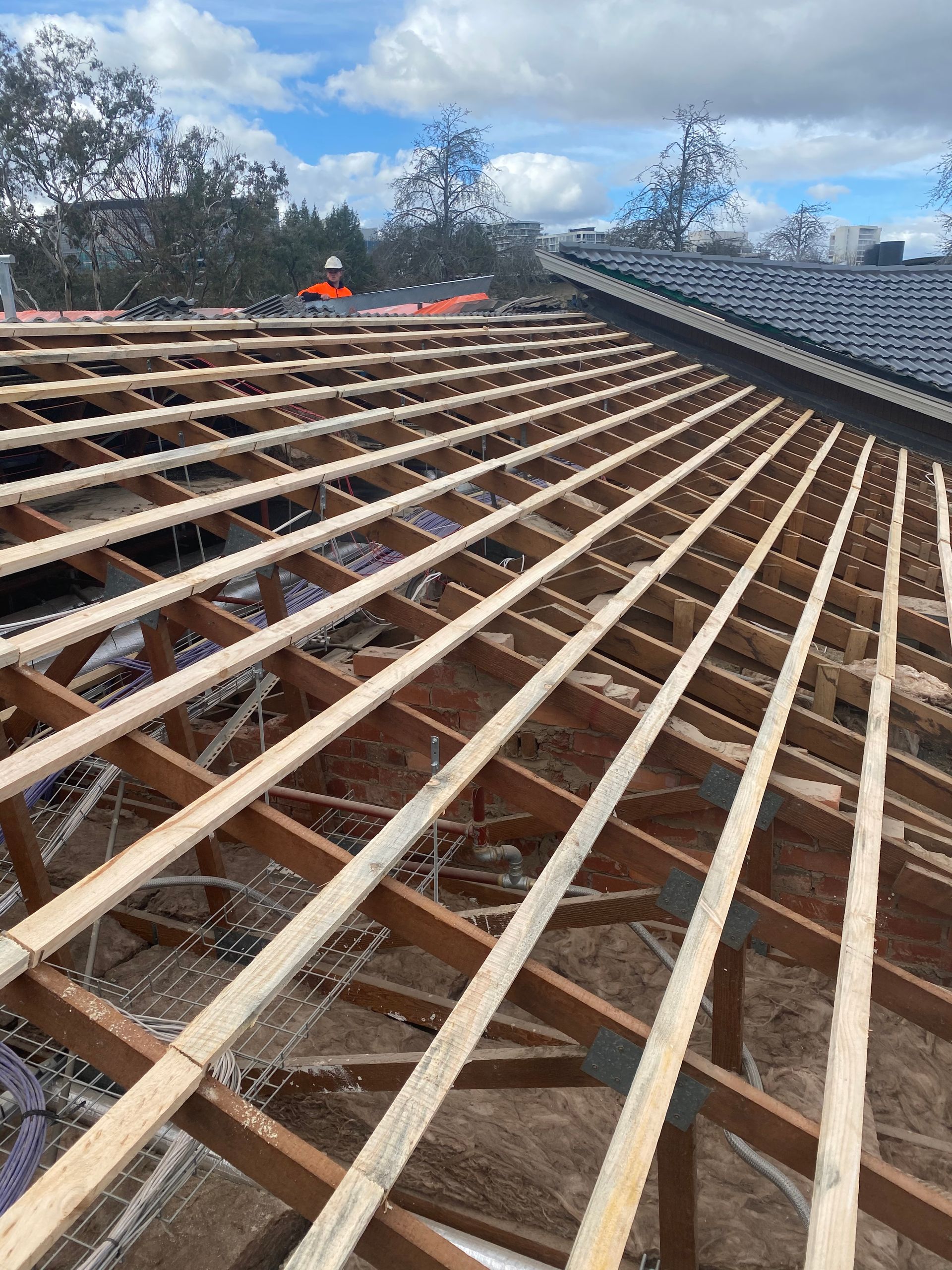 Roof framing with exposed wooden rafters under a blue sky with scattered clouds. — Boostn Pty Ltd in Glastonbury, QLD