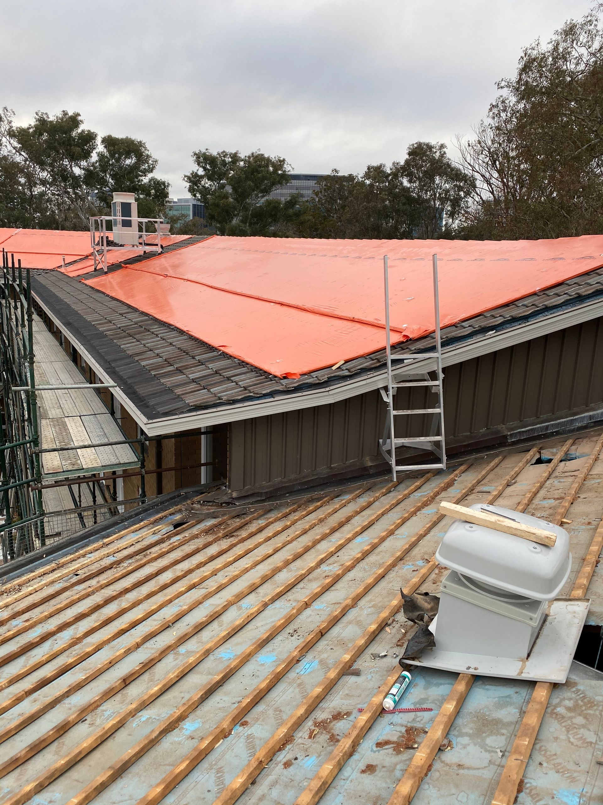 A partially roofed building under construction, with an orange tarp covering sections of the roof. — Boostn Pty Ltd in Glastonbury, QLD