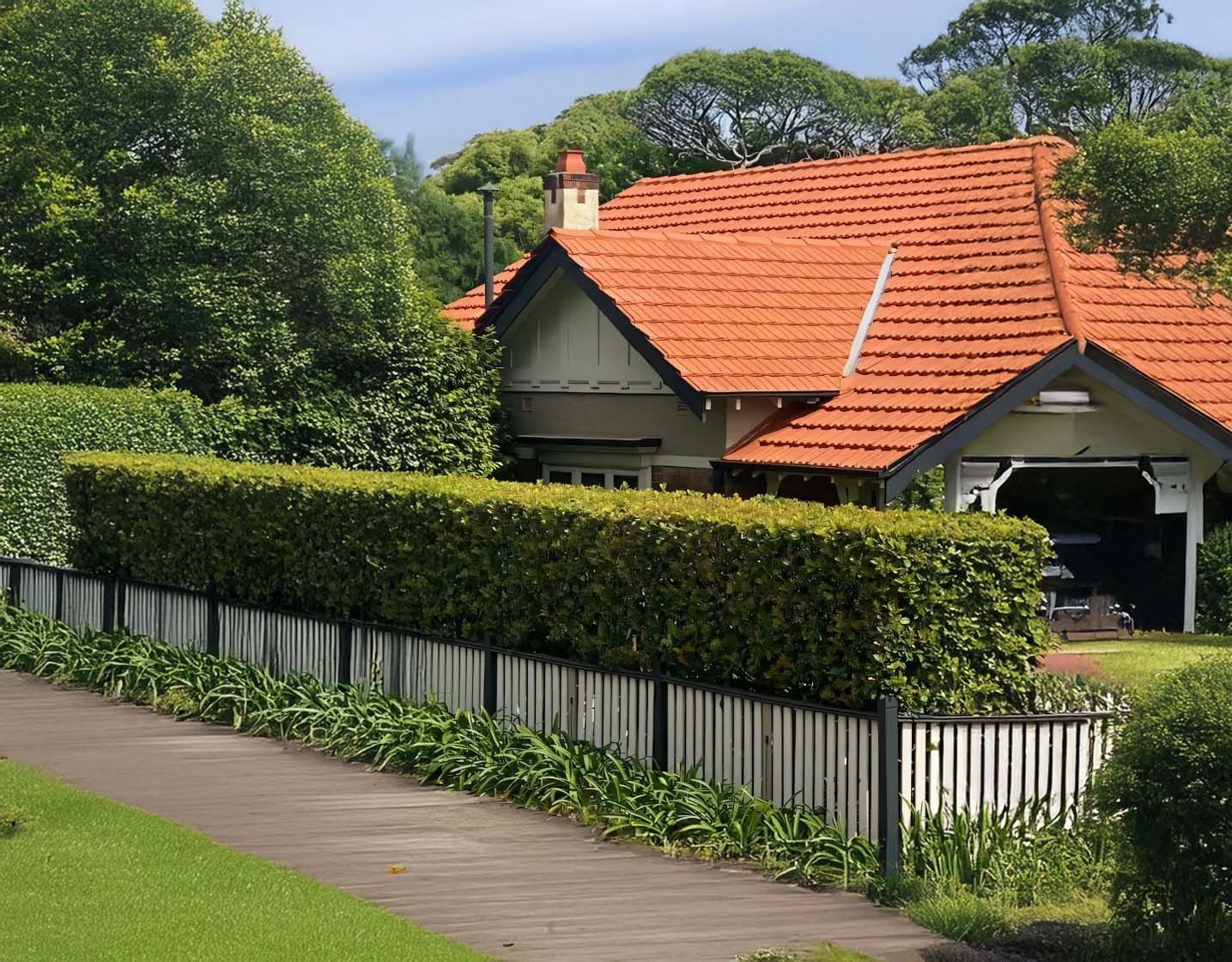 House with red tile roof, white fence, and green hedge.