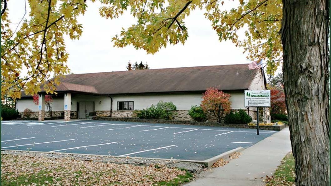 a white building with a brown roof is surrounded by trees and leaves