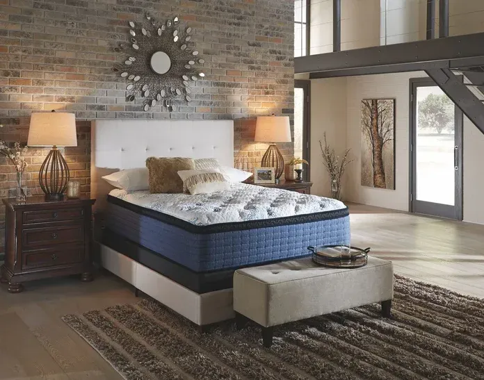 Bedroom with bed, nightstands, brick wall, artwork, and bench.