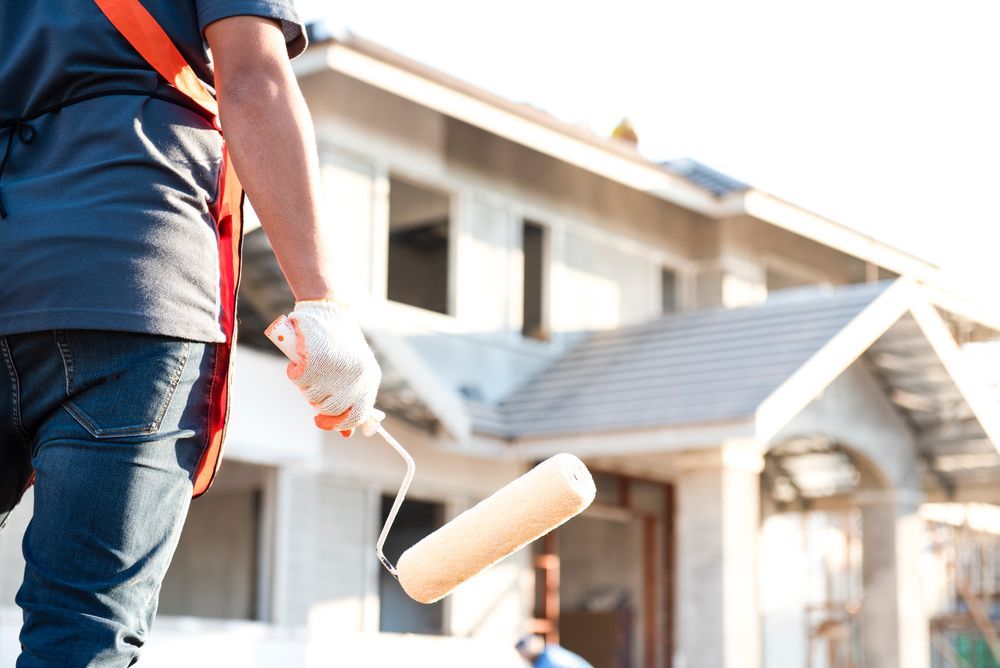 A man is holding a paint roller in front of a house.